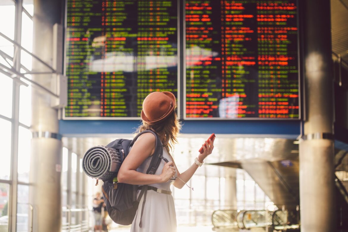 Solo woman traveller with backpack looking at the airplanes schedule chart on the big screens of airport