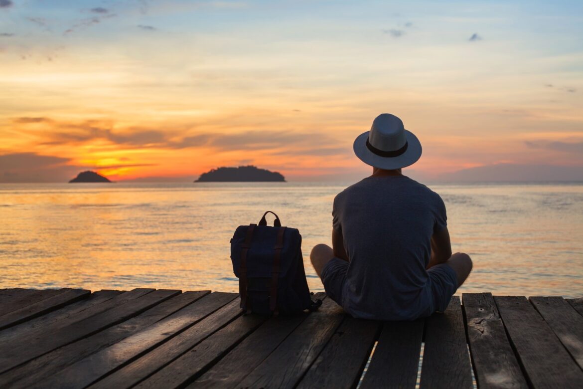 Male Solo Traveller sitting sea side enjoying the sunset
