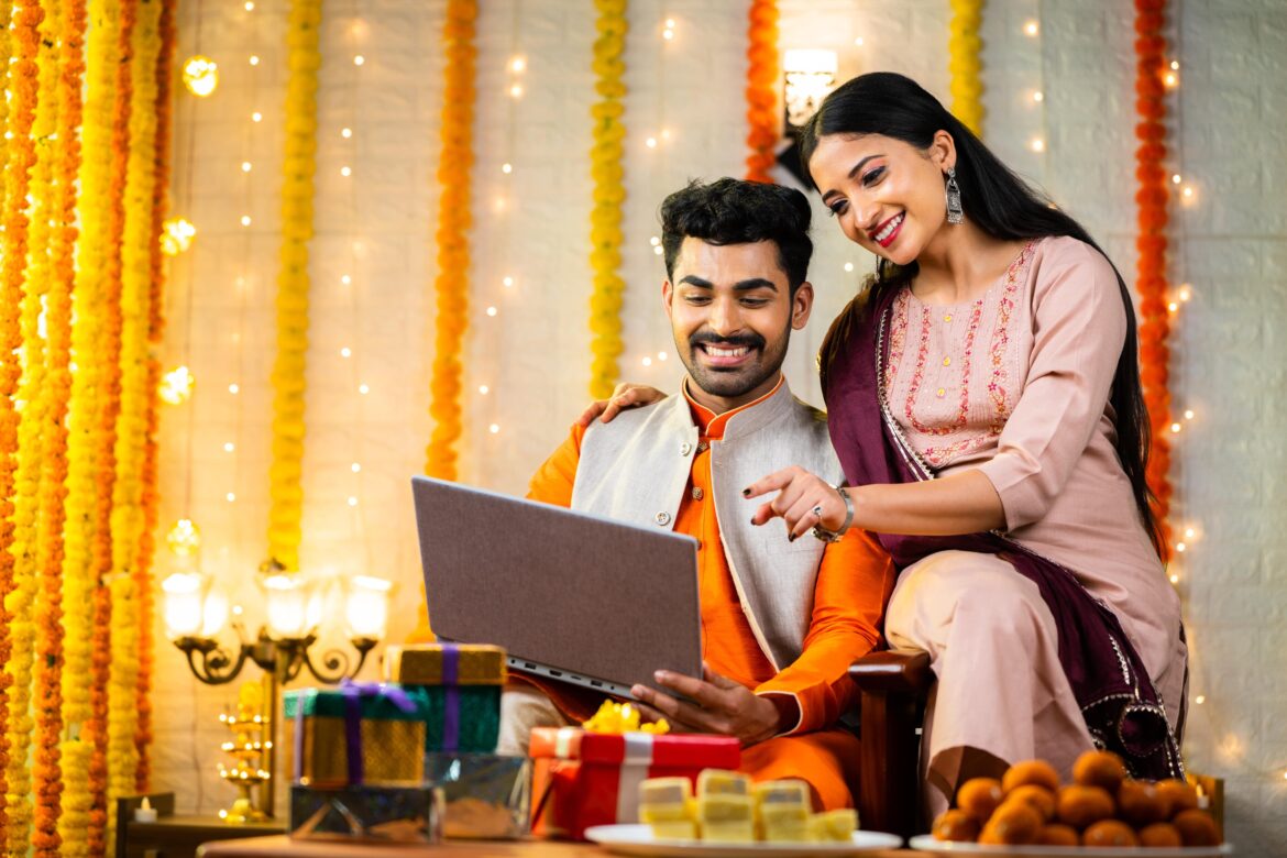 Happy young indian couple busy checking laptop during festival celebration at home, concept of online shopping from diwali sale on ecommerce websites