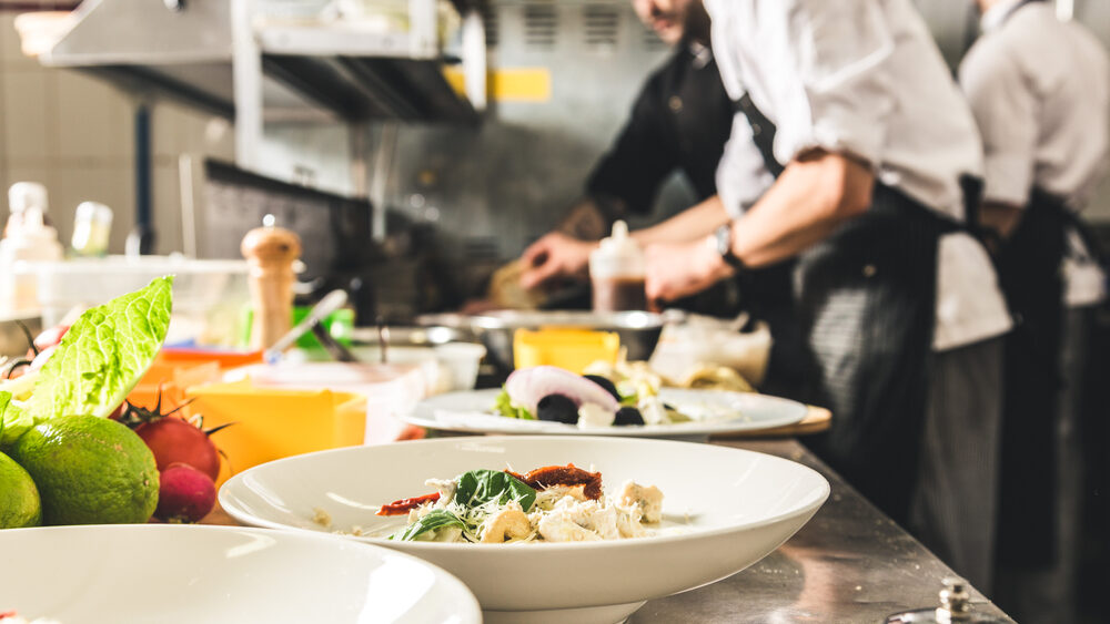 Professional chef cooking in the kitchen restaurant at the hotel, preparing dinner. A cook in an apron makes a salad of vegetables and pizza.
