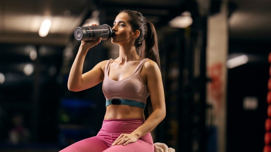 A thirsty and tired sportswoman is taking a break and drinking water in a gym.