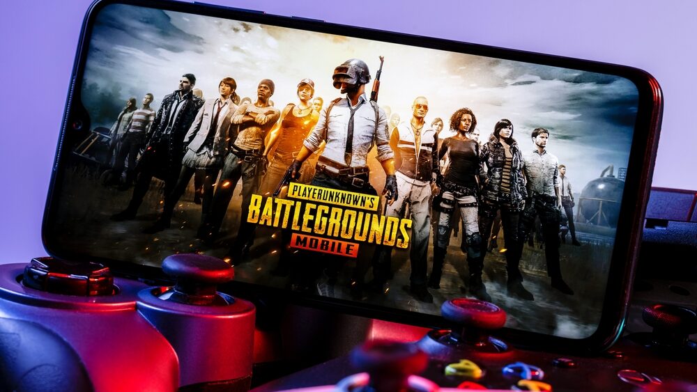 PlayerUnknown Battlegrounds (PUBG) is an online multiplayer battle royale game. A smartphone with the frame from PUBG Mobile on the pile of the gamepads.